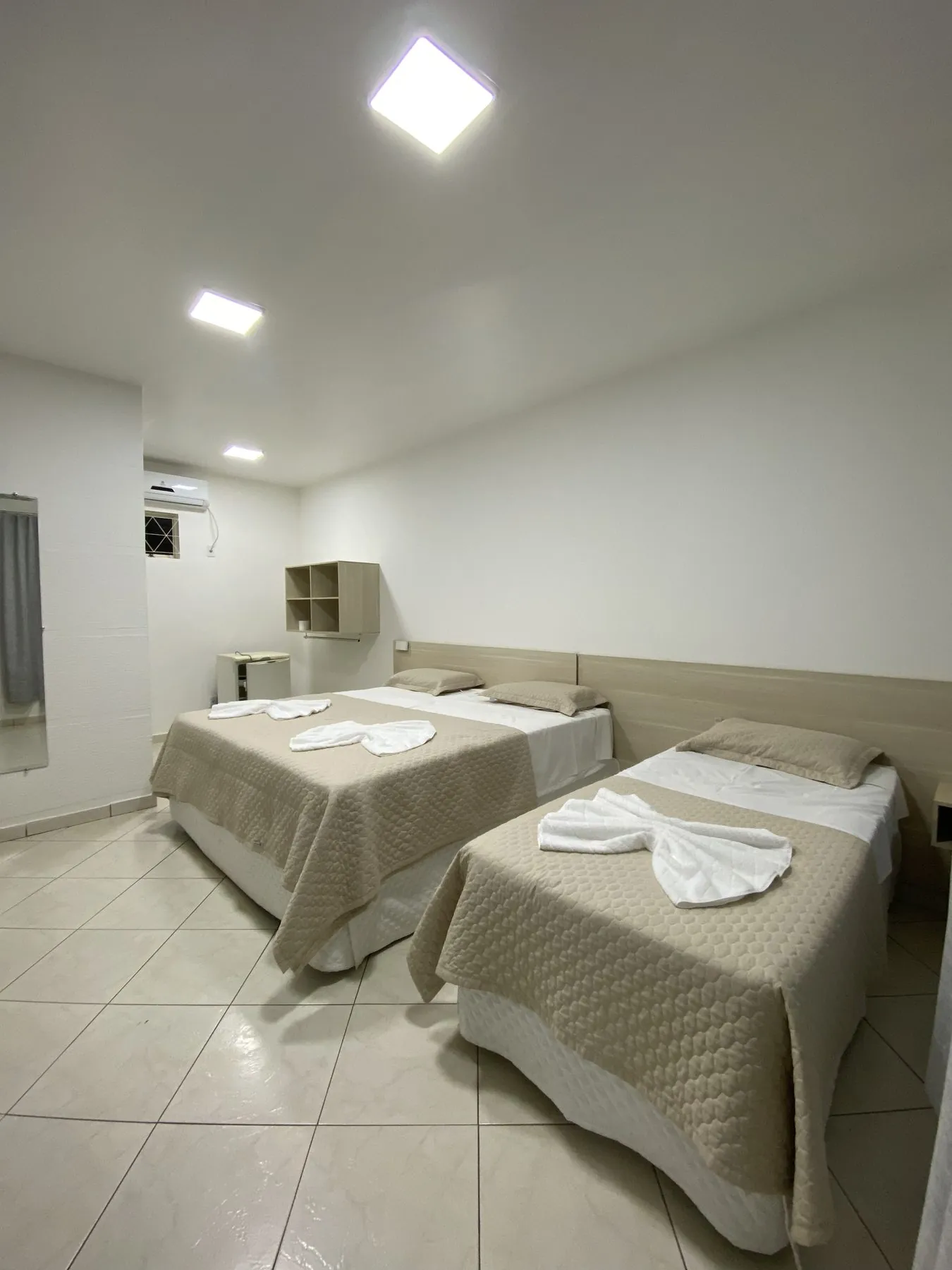 Quarto com duas camas arrumadas, toalhas sobre elas e o ar-condicionado no alto da parede.
