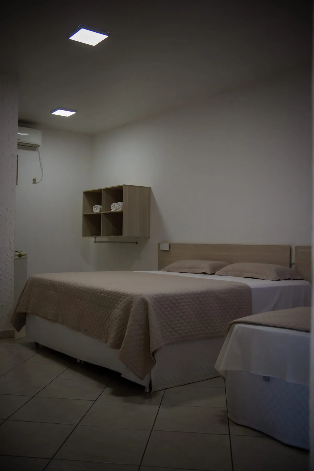 Quarto do Hotel Rosário com cama de casal arrumada e um nicho com toalhas na parede.