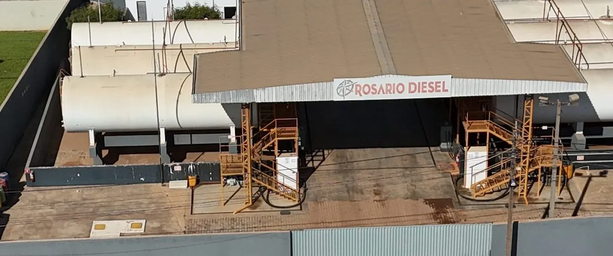 A plataforma de carregamento da base do TRR, coberta, com a placa Rosário Diesel, as escadas amarelas dos dois lados e os tanques deitados atrás.