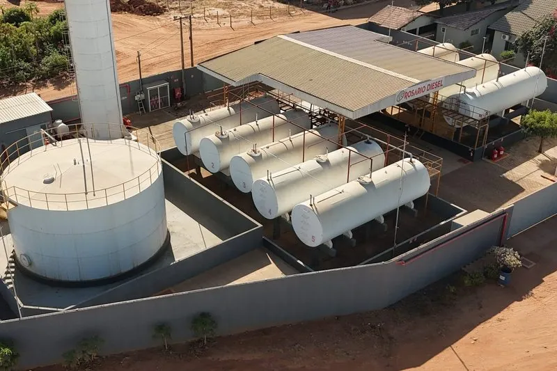 Tanques de armazenamento da base vistos do alto: um tanque redondo com escada amarela, a torre e a fila de tanques deitados.