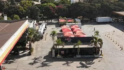 Vista do alto do Haru Joy Rosário: guarda-sóis vermelhos e palmeiras na frente da casa, com a cobertura do posto à esquerda.