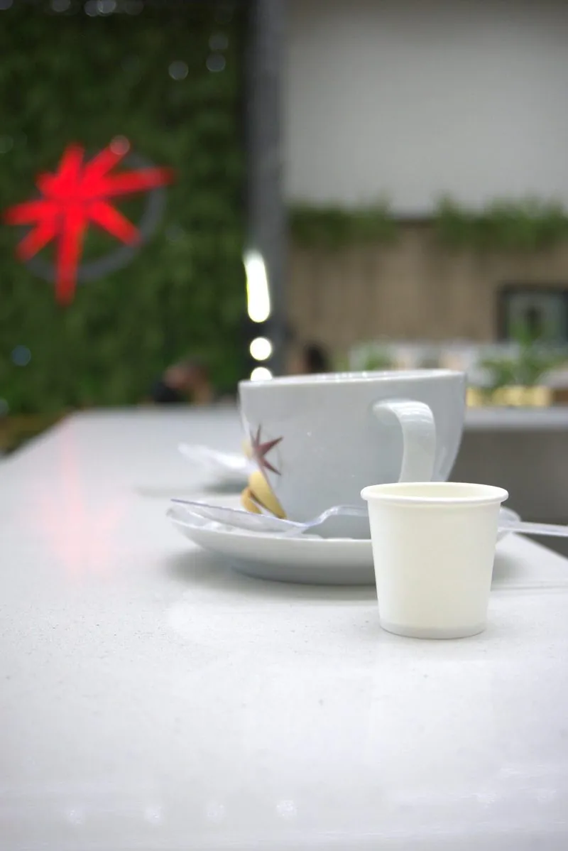 Xícara de café numa mesa branca do Rosário Premium, com a estrela vermelha desfocada ao fundo.