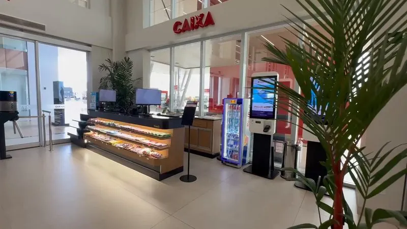 Caixa da conveniência do Rosário Premium, com o balcão de doces iluminado, um totem de autoatendimento e o letreiro CAIXA.