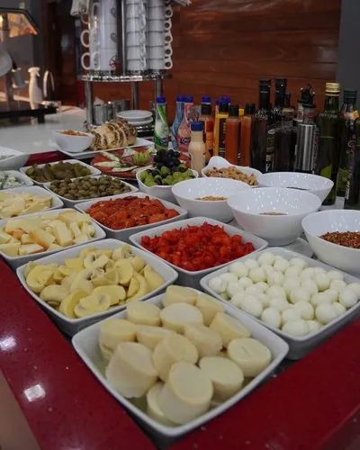 Buffet frio do Restaurante Rosário: queijos, palmito, cogumelos, tomate seco, ovos de codorna e azeitonas em travessas sobre a bancada vermelha.