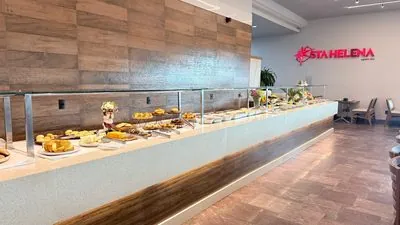Buffet comprido do Restaurante Santa Helena, com pães e bolos no balcão e o letreiro STA HELENA vermelho na parede.