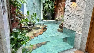 Jardim interno com plantas, pedras e um espelho d’água de azulejos verdes.