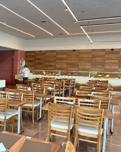 Salão do Restaurante Santa Helena com mesas e cadeiras de madeira e o buffet ao fundo.