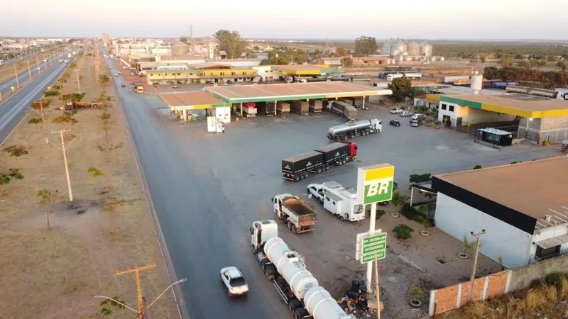 O Posto Santa Helena LEM visto do alto no fim da tarde: a pista com cobertura, caminhões no pátio, a placa BR do posto e a rodovia.