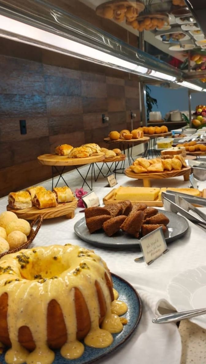Mesa de café da manhã com bolo de maracujá, pão de queijo, folhados e pães