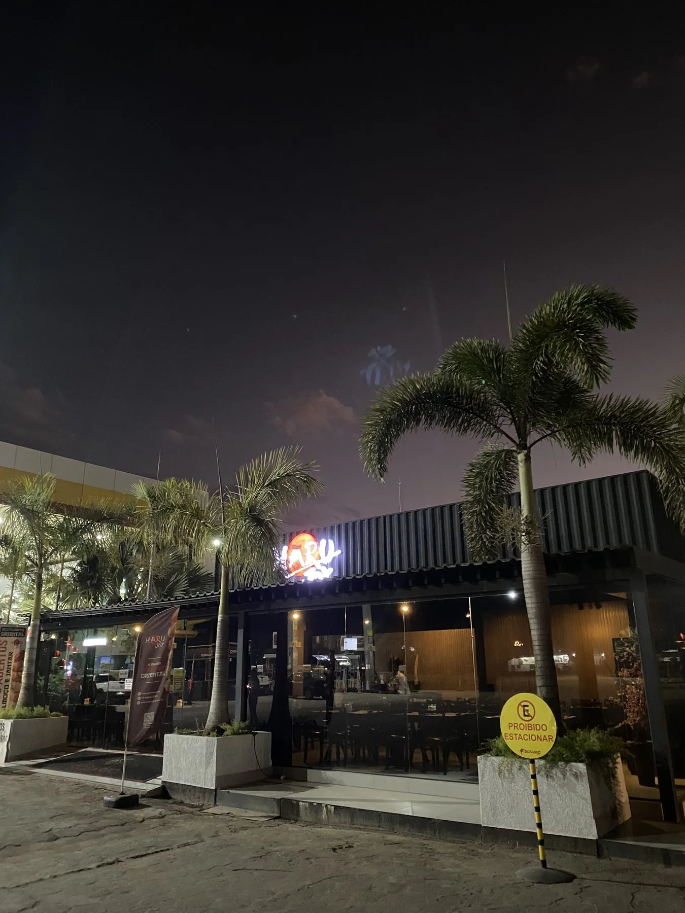 Fachada do Haru Joy Rosário à noite, entre palmeiras.
