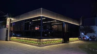 O Haru Joy Premium à noite: o letreiro vertical aceso na quina, as paredes de vidro e a faixa de luz sobre os canteiros.