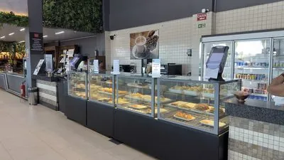 Estufas de vidro com salgados e doces no balcão do café, com o quadro de bebidas na parede.