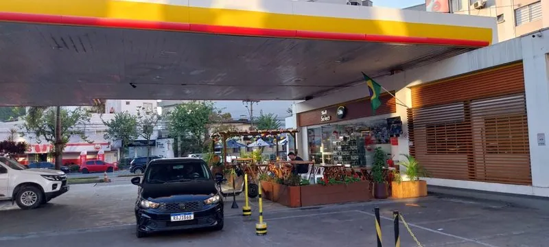 Frente da loja Shell Select do Posto San Marino, com plantas e mesas.