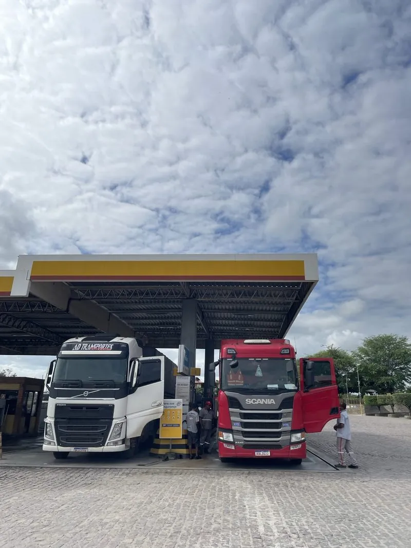 Carretas sob a cobertura Shell do Posto Santa Helena, com céu de nuvens.