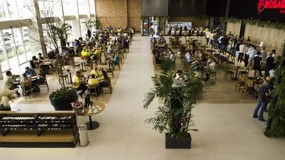 Corredor largo da praça de alimentação do Restaurante Premium, com palmeiras em vasos e as mesas cheias dos dois lados.