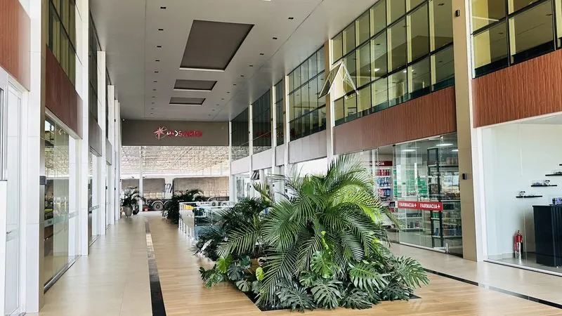 Galeria interna do Rosário Premium: corredor largo entre lojas, com um canteiro de plantas.